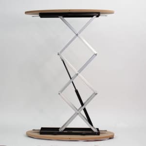 A portable display counter with a round wooden top and a silver folding support structure.