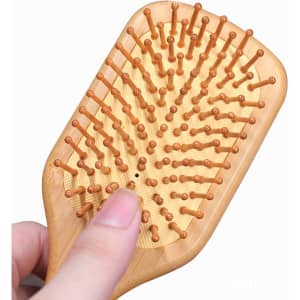 A bamboo hair brush featuring wooden pins and a natural finish, held in a hand.