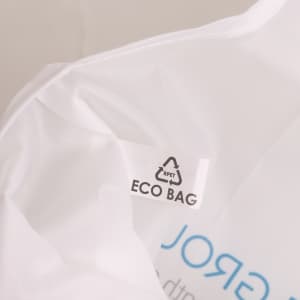 A close-up of a white foldable shopping bag with a logo and eco-friendly label inside.