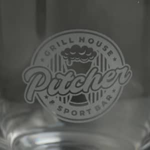 A glass featuring a logo for a grill house and sport bar, presented in clear glass with a decorative design.