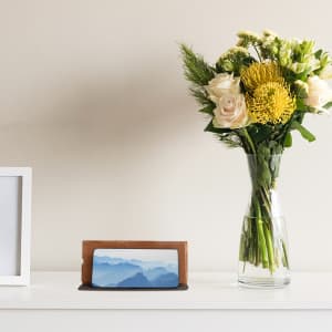 A foldable cork wireless charger in a natural wood finish, placed beside a vase of flowers on a shelf.