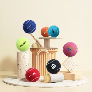 A collection of colourful pet tennis balls in various shades, with some featuring logos, displayed on a minimalistic pedestal.