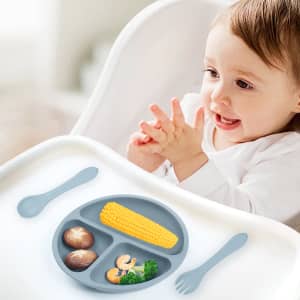 A silicone kids suction plate in grey with sections for food, alongside a spoon and fork.