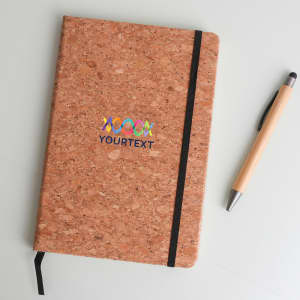 A cork notebook with a black elastic band and a pen next to it, featuring colourful branding on the cover.