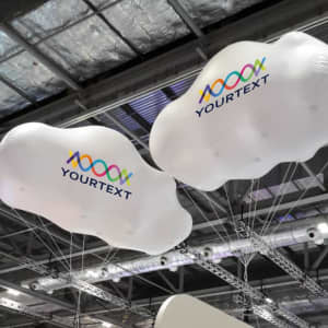 Two large white inflatable clouds with a logo, suspended from the ceiling at an exhibition event.