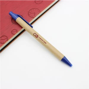A Kraft Paper Pen with a blue tip and clip, placed on a red notebook with a clock design. Features a logo.