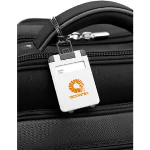 A white ABS luggage tag attached to a black suitcase with a logo. The tag has spaces for a name and address.