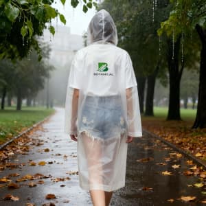 A clear, reusable adult raincoat with a hood, worn over denim shorts, in a park during light rain.