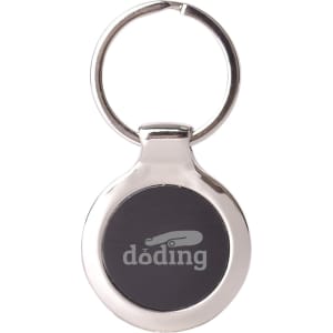 A metallic keyring with a circular design and a dark central area, featuring a branding logo.