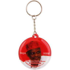 A red PVC LED keyring featuring a circular design and an image of a person, along with a branding logo.