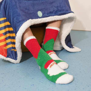 Crew Custom Pattern Coral Fleece Socks in red, green, and white, worn by a person sitting under a blanket.