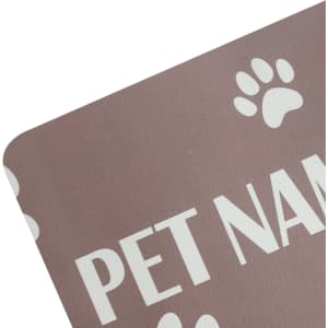 A pet feeding mat in a soft brown shade with white paw print designs and text. It features a branding logo.