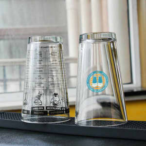 A set of clear glass tumblers, one featuring a design with text and a logo, the other is plain.