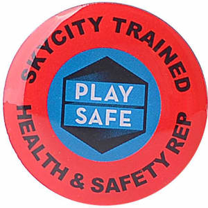 A red lapel pin featuring a circular design with a logo and text in blue and black.