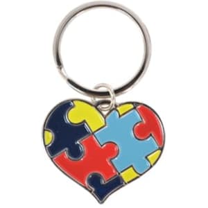 A heart-shaped keyring featuring red, blue, yellow, and black puzzle piece designs, attached to a metal ring.