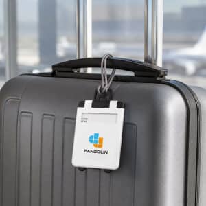 A white ABS luggage tag attached to a grey suitcase, featuring a logo and adjustable strap.