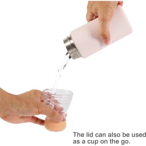 A drink bottle in soft pink, pouring liquid into a clear cup. It has a stainless steel lid that doubles as a cup.