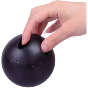 A black, bowling ball-shaped stress reliever with two finger holes is being held by a hand.