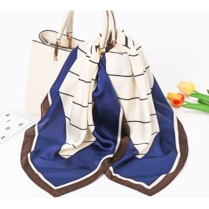 A silk chiffon scarf featuring a blue and cream geometric pattern, displayed draped over a handbag.