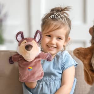 A plush wolf hand puppet in brown and beige, held by a smiling child sitting on a couch.