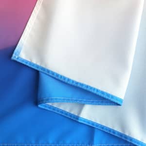 A large table runner featuring a gradient design with shades of blue and white. It has a stitched edge and branding.