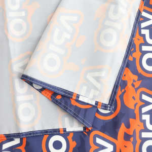 A small table runner featuring a vibrant pattern in orange and navy, with a prominent logo and neat stitching.