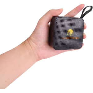 A portable black wireless Bluetooth speaker held in a hand, featuring a branded logo on the front.