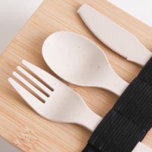 A bamboo-covered lunch box with light-coloured utensils laid on top, secured with a black strap.