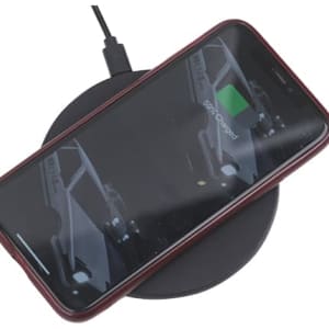 A black wireless charger with a smartphone placed on top, connected to a power source.