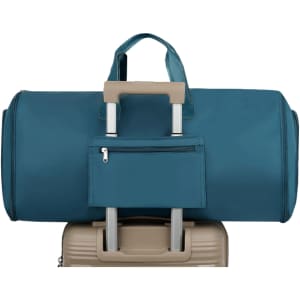 A teal duffel bag sits atop a beige suitcase, featuring a small zippered pocket on the front.