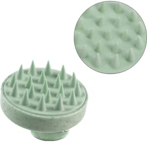 A green hair scalp massager with textured spikes for stimulating the scalp, featuring a circular design.