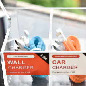 A clear acrylic display with two compartments, featuring blue and orange charging cables and labels for wall and car chargers.