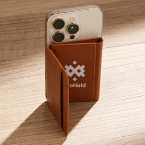 A brown PU magnetic wallet paired with a smartphone, set against a wooden surface. The wallet features a logo.