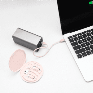 A silver power bank connected to a laptop, alongside a round, pink cable kit containing various connectors.
