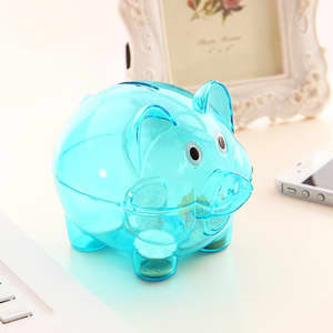 A transparent blue piggy coin bank with cartoonish features, placed on a desk alongside a phone and laptop.