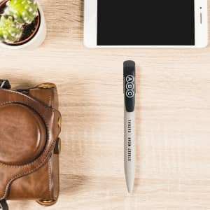 A wheat straw click pen in grey with a black grip, placed beside a smartphone and a brown leather bag.