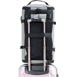 A grey convertible bucket backpack duffel bag with a black mesh pocket and retractable handles, attached to a suitcase.