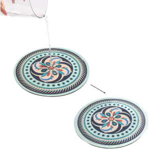 A round, absorbent trivet features a floral design in blue, pink, and cream, with a contrasting black border.