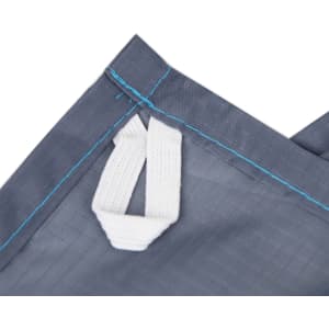 A close-up of a grey picnic blanket featuring a white handle and blue stitching, with a logo present.