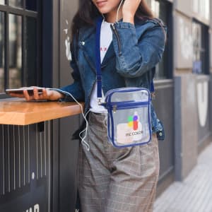 A clear crossbody tote bag with blue accents, featuring a zipper closure and an attached logo.