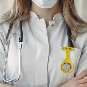 A yellow silicone nurse watch attached to a white lab coat, alongside a stethoscope.
