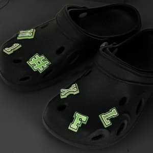 Black clog shoes adorned with green glowing charm letters and symbols for a fun and novelty look.