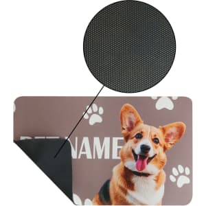 A pet feeding mat in brown featuring a smiling dog design and paw prints, with a textured black backing.