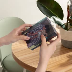 A hands holding a transparent 3D cube featuring colourful images on its sides, placed on a wooden table near a plant.