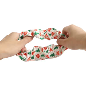 A hair scrunchie featuring a festive design with red snowflakes and green trees. It has a soft, stretchy fabric.