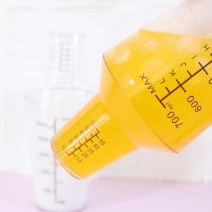 A drink bottle in orange and clear with measurement markings, featuring a measuring cap. It has a logo.