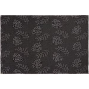 A plush floor mat featuring a dark grey floral pattern, with a subtle logo in the design.
