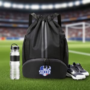 A black drawstring backpack with a bottom compartment, water bottle, and a pair of shoes on a grassy field.