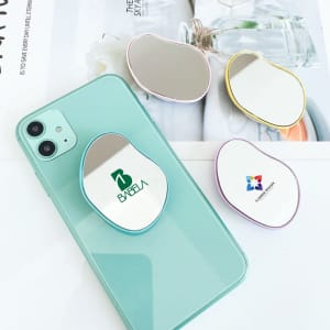 A custom-shaped mirror phone pop holder in various colours, featuring a logo on one design, placed on a mint phone.