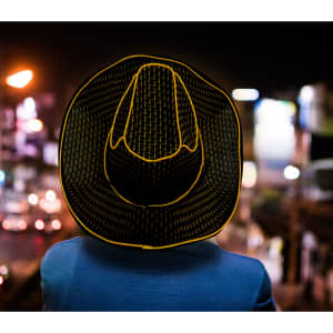 A person wearing a yellow and black striped straw hat with illuminated edges, set against a night-time background.